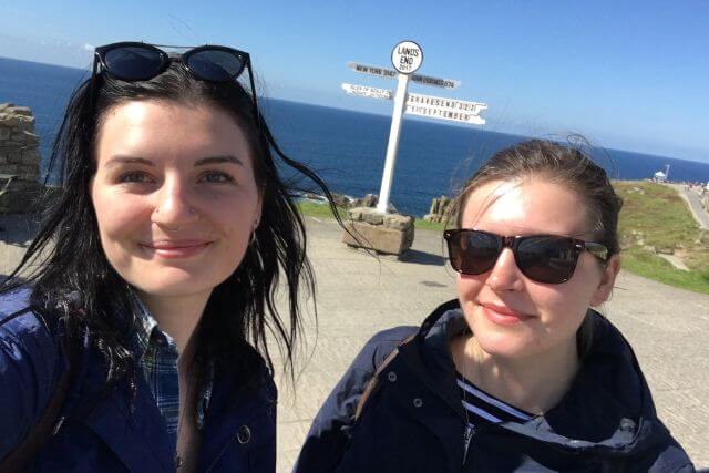 Two women posing for a selfie in front of the Land's End sign with the sea in the background.