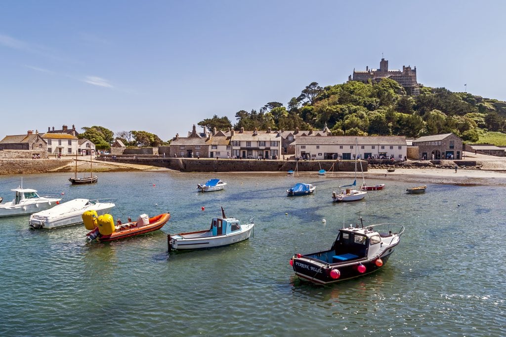 View towards St Michaels Mount Cornwall. Boats can be seen in the harbour and people can be seen on the promenade.