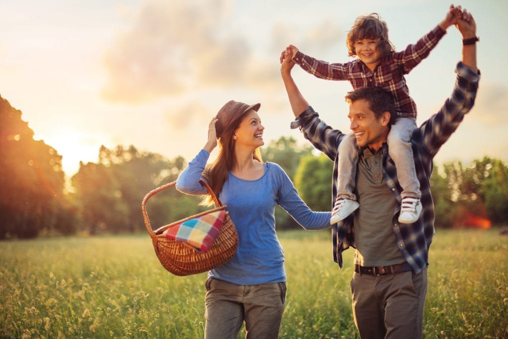 Picture of a young happy family walking across field going for picnic in gardens.