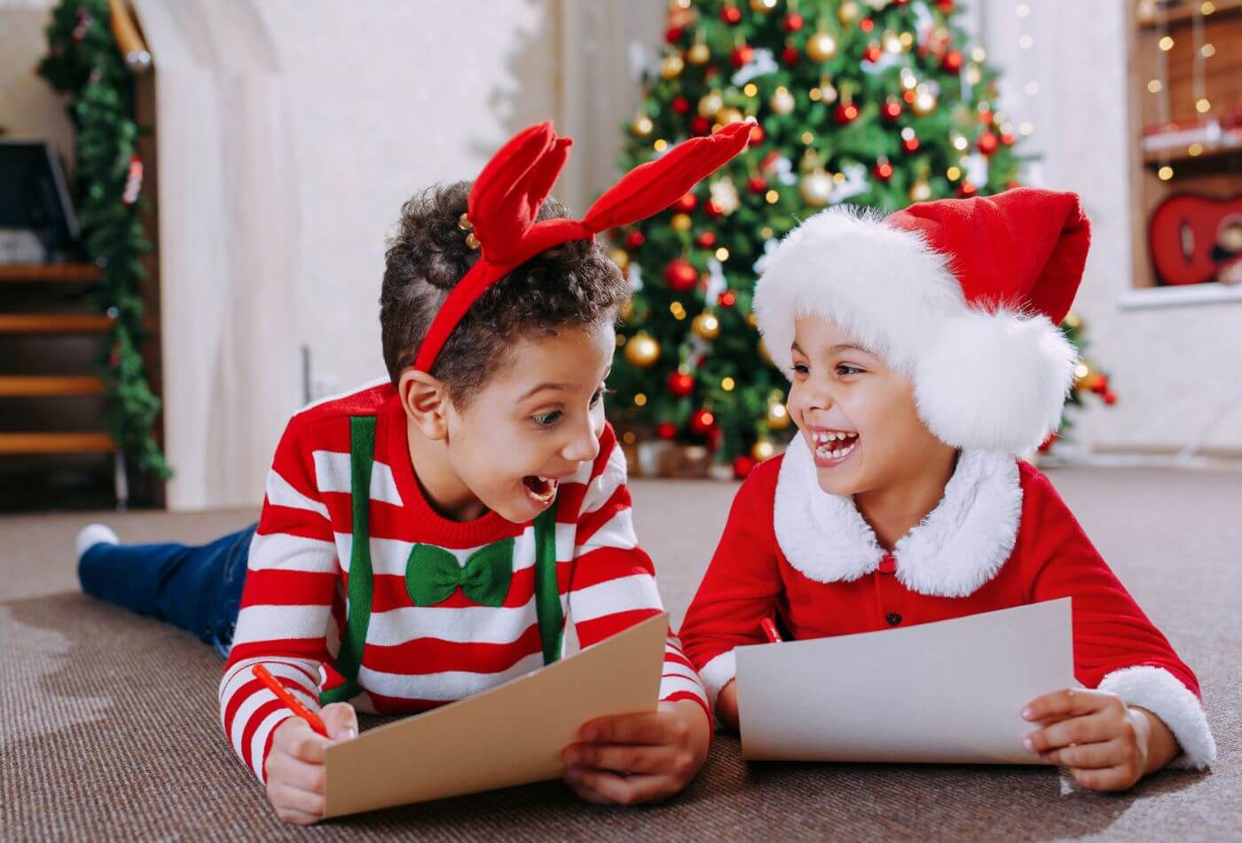Two children in festive outfits writing Christmas lists.