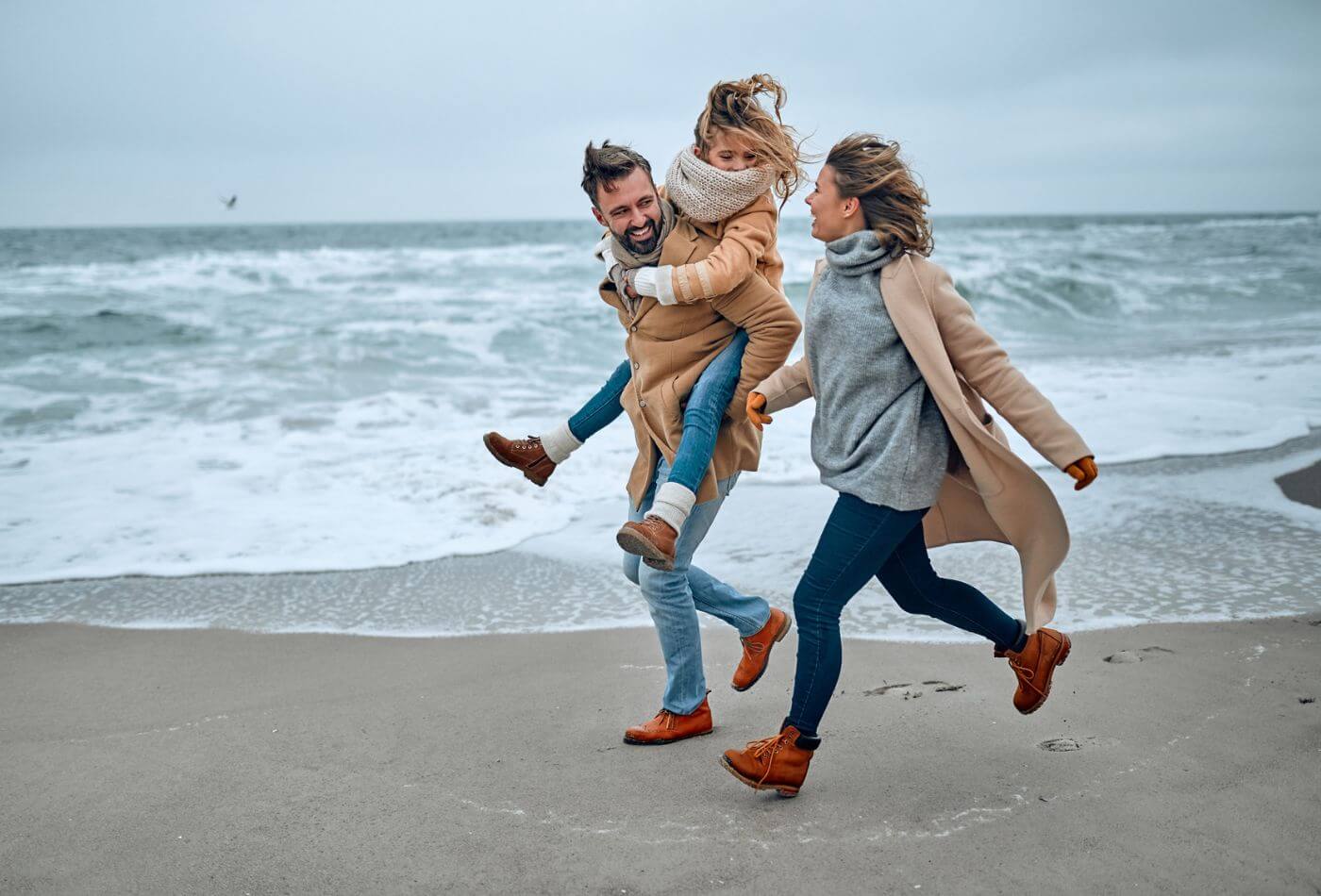 Portrait of a young married couple and their cute daughter who have fun on the beach in winter.