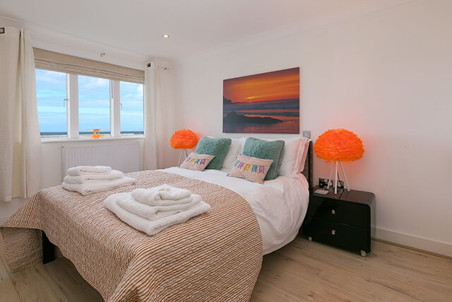 Sea view bedroom with double bed and local artwork on the wall.