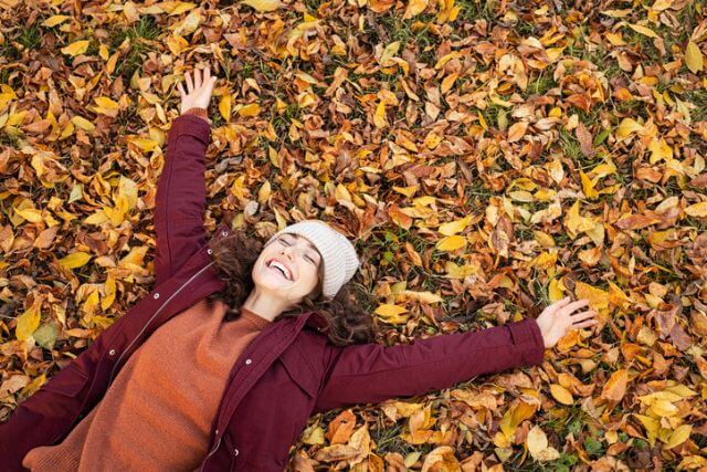 Woman dressed in winter clothes lying on autumn leaves.