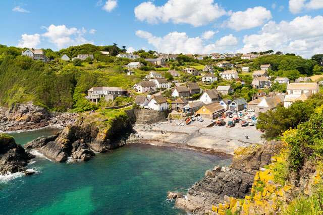 Cadgwith Cove on a sunny day, a small bay with sea on one side and houses and greenery on the other
